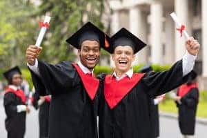 Two young students wearing gowns and tassels expressing happiness by raising hands