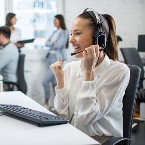 A cheerful young customer support representative wearing a headset and answering calls at her desk