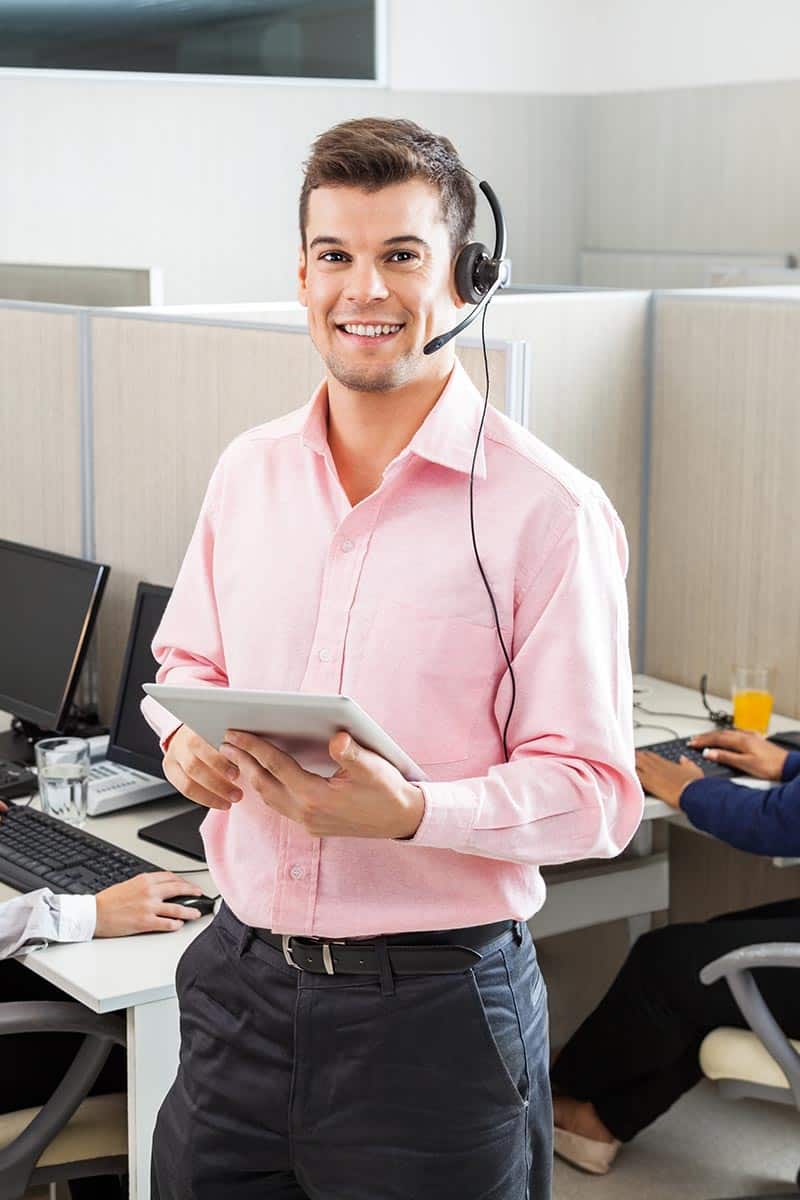 A smiling male employee wearing a headset with a tablet in his hands facing the camera